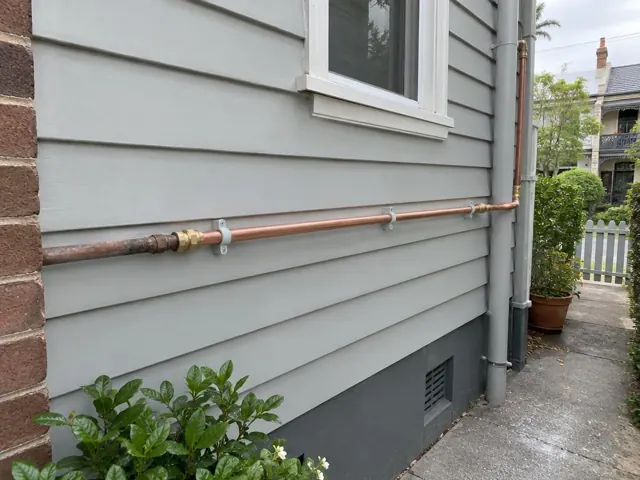 Copper water pipe repaired along a weatherboard exterior wall with brackets in Double Bay