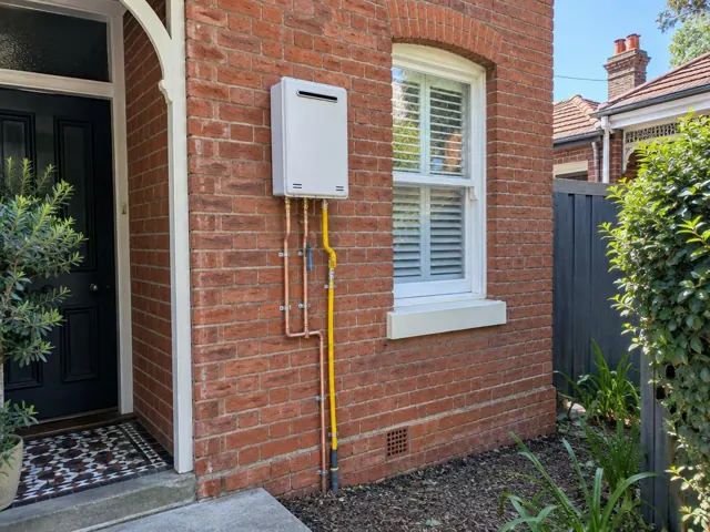 Wall-mounted hot water unit on a brick exterior wall beside a window in Edgecliff