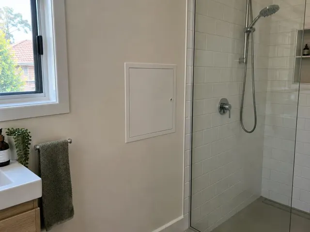 Bathroom wall with a small access panel beside a tiled shower and vanity in Rose Bay